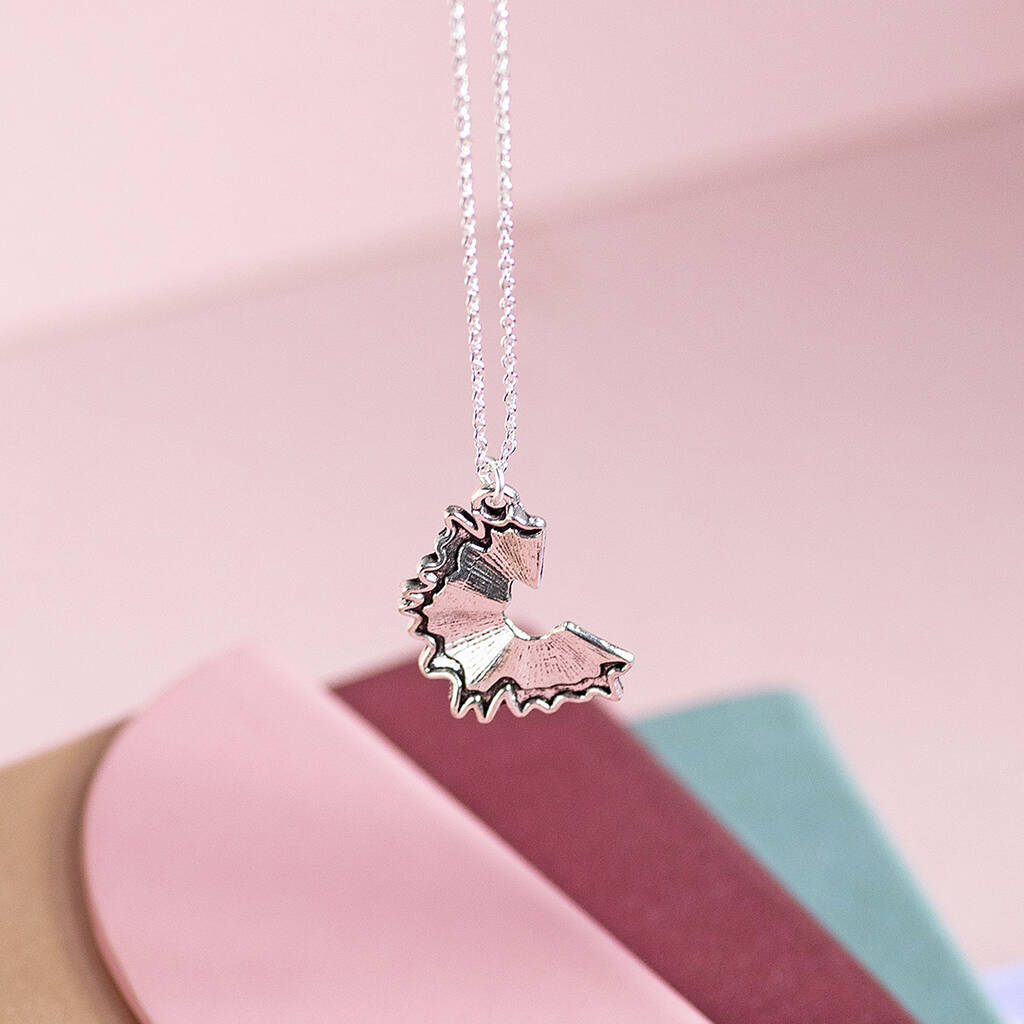 Silver pencil shaving pendant necklace suspended above pastel stationery, playful statement jewellery design