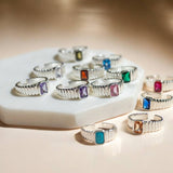 Silver plated ribbed birthstone rings in all 12 birthstone months displayed on a marble display.