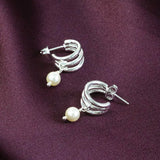 Image shows Silver Plated Triple Hoop Pearl Earrings on a maroon backdrop