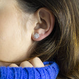 Image shows silver plated snowflake charm stud earrings worn in the ear.