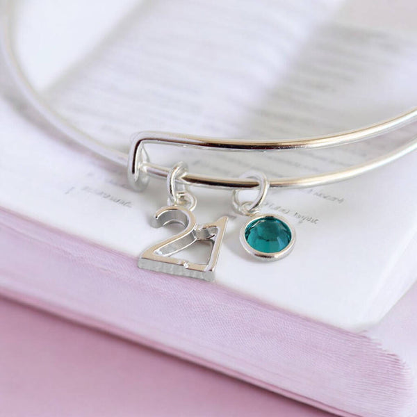 Silver birthday charm bangle featuring a 21 pendant and teal birthstone crystal detail