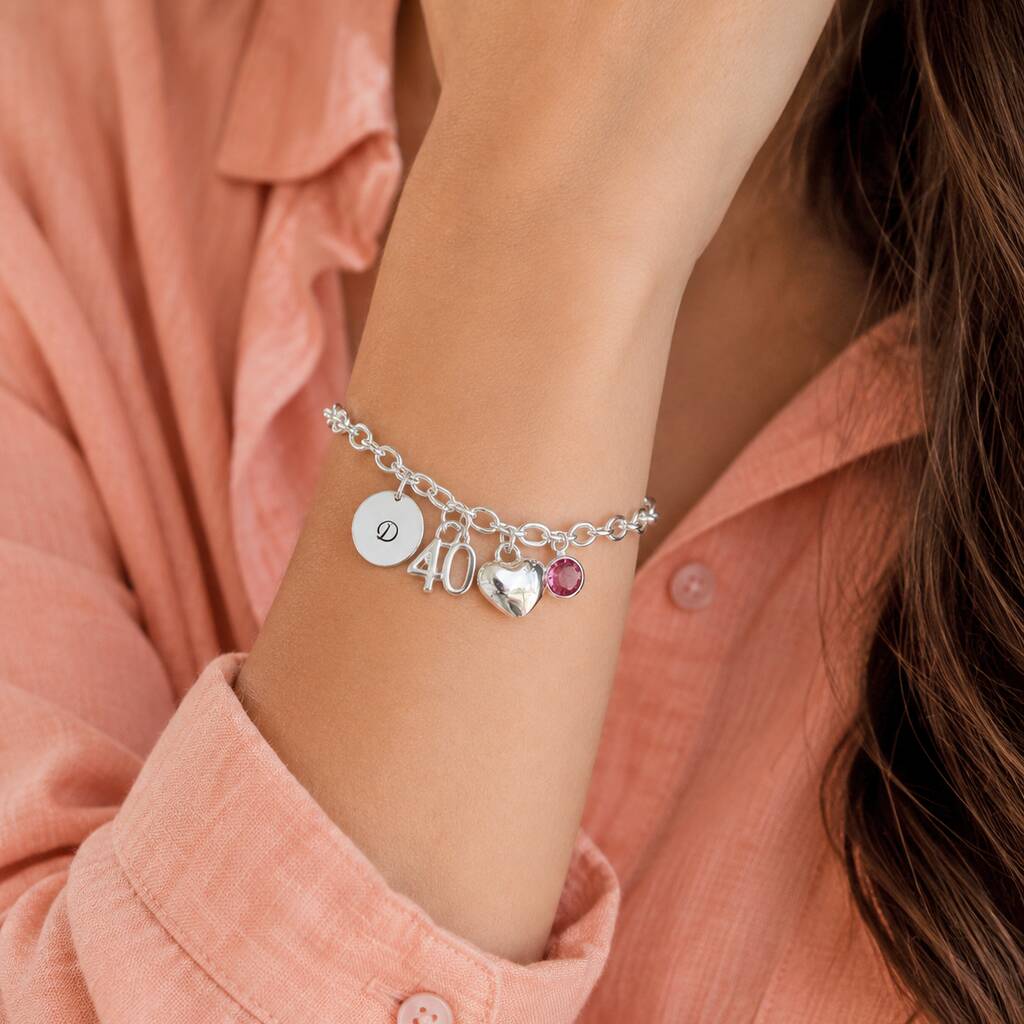 Silver charm bracelet styled with an initial disc, 40 charm, heart charm and pink crystal birthstone