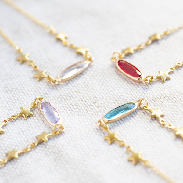 Image shows four Star Chain Bracelets with Birthstone Detail from left to right: April Crystal, Ruby July, June Light Amethyst and December blue zircon sitting on a white backdrop.
