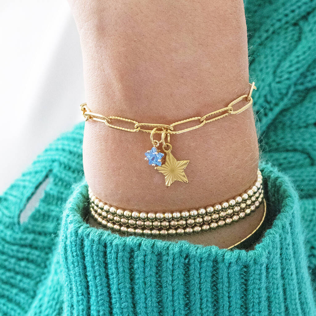 Image shows model in turquoise cardigan wearing a gold plated star charm bracelet with star birthstone detail.