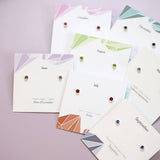 Colourful sterling silver birthstone studs in ruby, sapphire and other shades, displayed on monthly jewellery cards.
