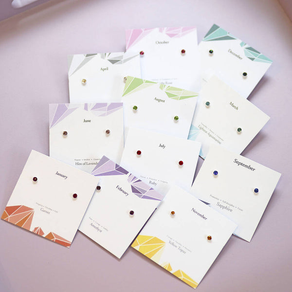 Rainbow birthstone stud earrings in sterling silver, arranged on colourful month cards from January to November.
