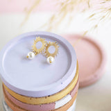 Image shows Sun Earrings with Pearl Drop Detail on a purple dish.