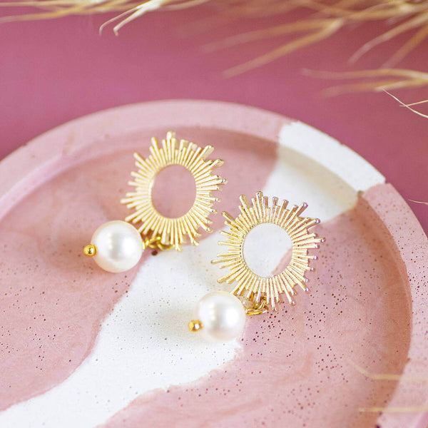 image shows Sun Earrings with Pearl Drop Detail on a pink backdrop.