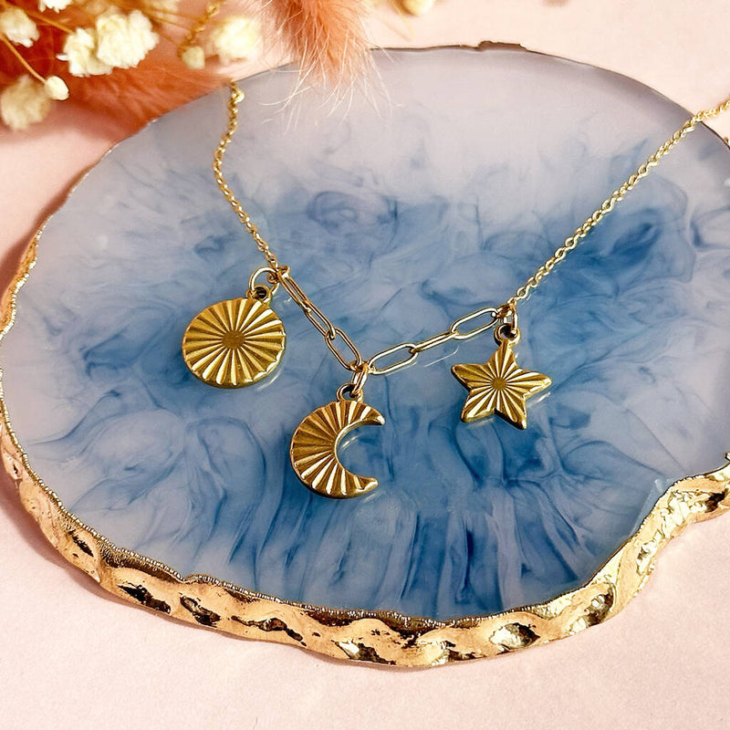 Image shows sun moon and star necklace in gold placed on a blue trinket dish
