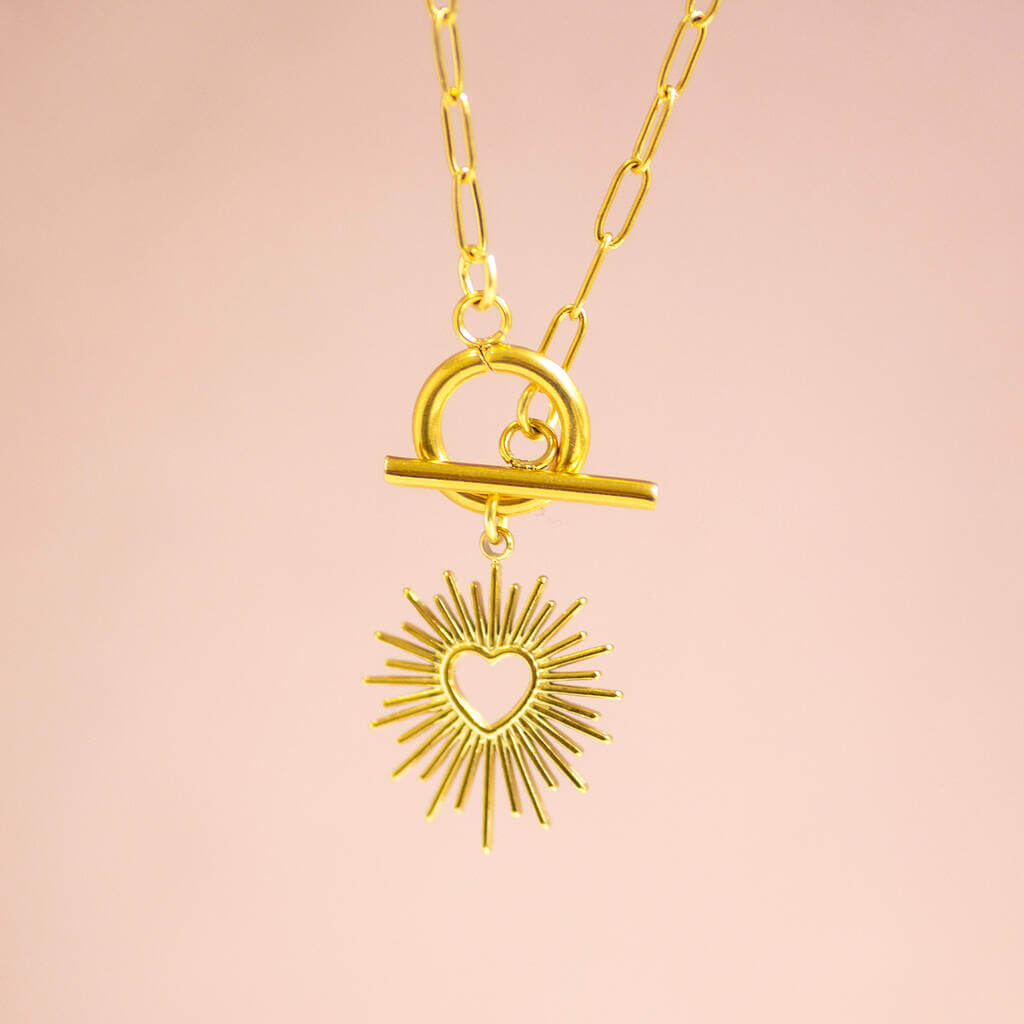 A gold sunburst charm suspended from a gold toggle necklace on a paperclip style chain