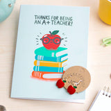Close-up of Thank You Teacher card and red apple earrings displayed on a desk