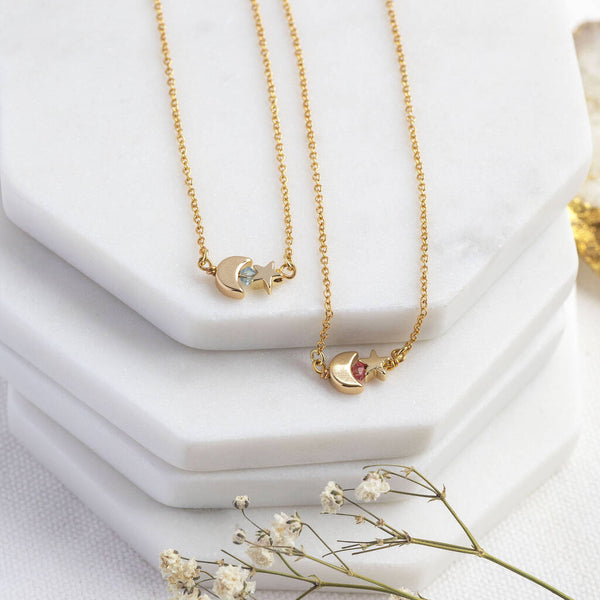 Image shows two Tiny Moon and Star Necklaces with Birthstone Detail from left: March Aquamarine and October Rose. Sitting on a white jewellery stand backdrop.