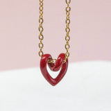 Image shows gold plated Tiny Red Enamel Floating Heart Necklace on a pink backdrop.