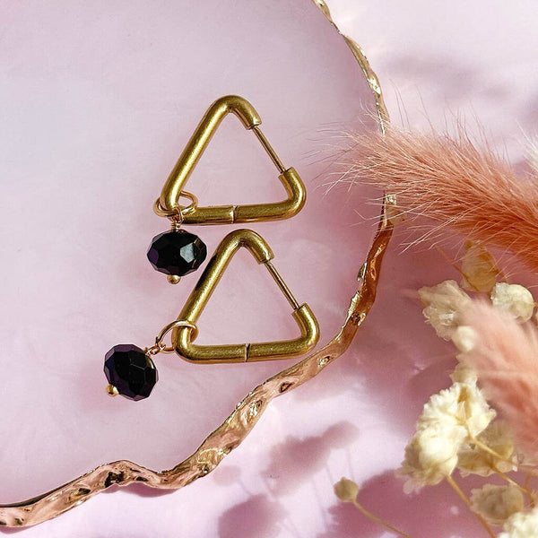 Image shows Triangle Huggie Earrings with Black Crystal Charms on a pink backdrop