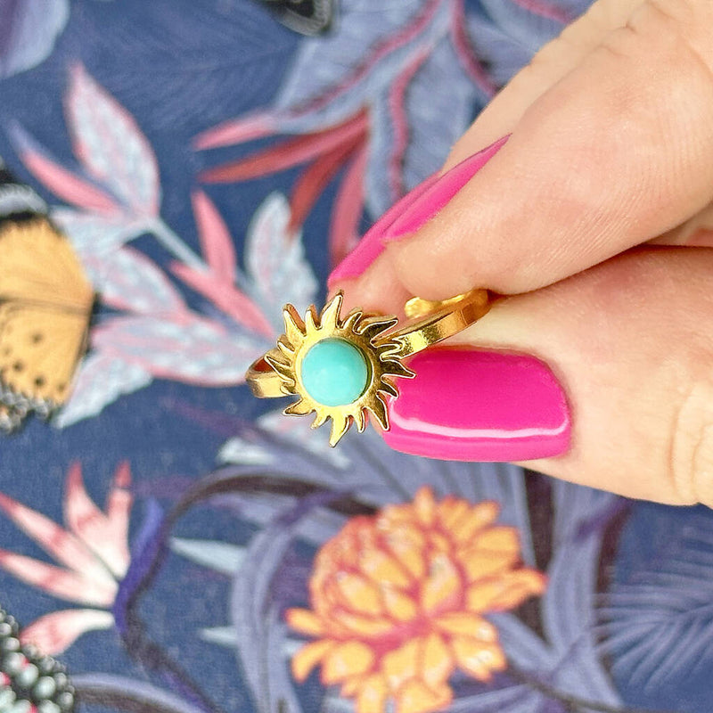 Image shows hand with bright pink nail polish holding a turquoise gemstone sun ring