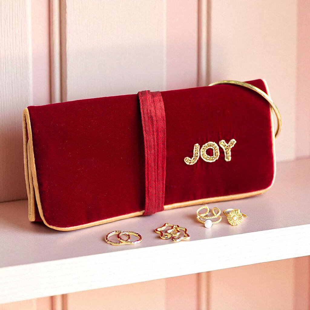 Maroon velvet and gold piped  jewellery roll with beaded ‘JOY’ detail, styled with jewellery pieces.