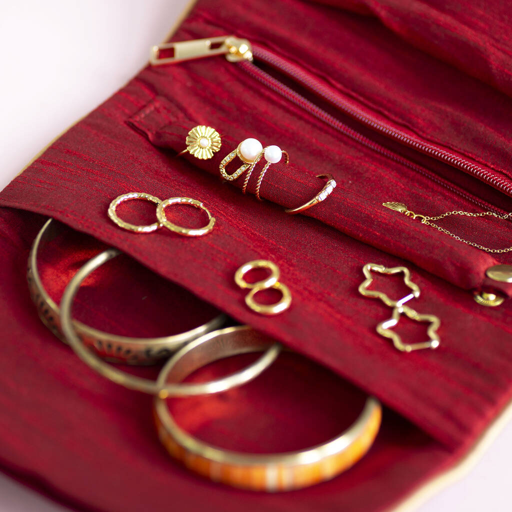 Open velvet jewellery roll in maroon velvet and gold zip showing compartments for rings, earrings, and necklaces.