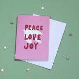 Pink card with 'Peace Love Joy' text on a green background with stars