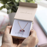 Image shows rose gold family birthstone necklace with three birthstones on a 'mum' sentiment card inside the JOY by Corrine Smith branded gift box.