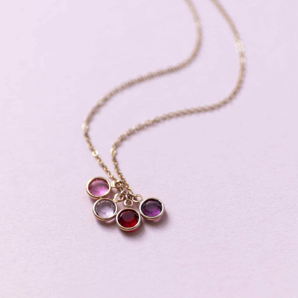 Image shows rose gold family birthstone charm necklace with four swarovski crystal birthstones on a pink backdrop.