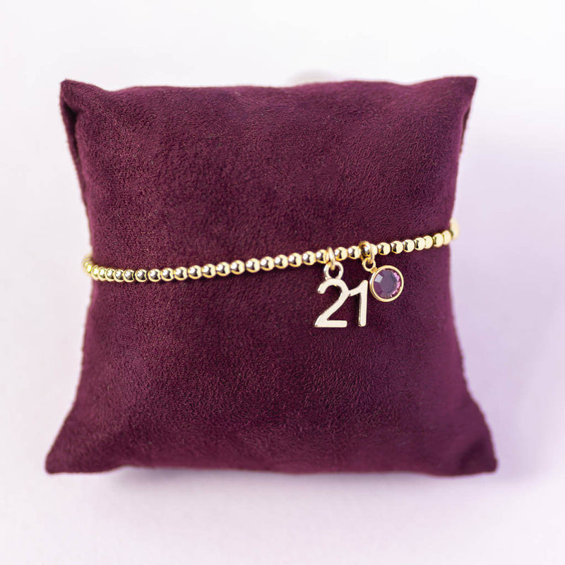Image shows gold plated 21st birthday birthstone beaded bracelet with a '21' charm and a February amethyst Swarovski Crystal.