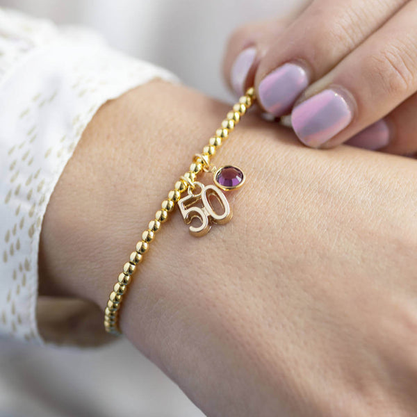 model wears gold plated 50th birthday birthstone charm bracelet with '50' charm and Swarovski birthstone crystal