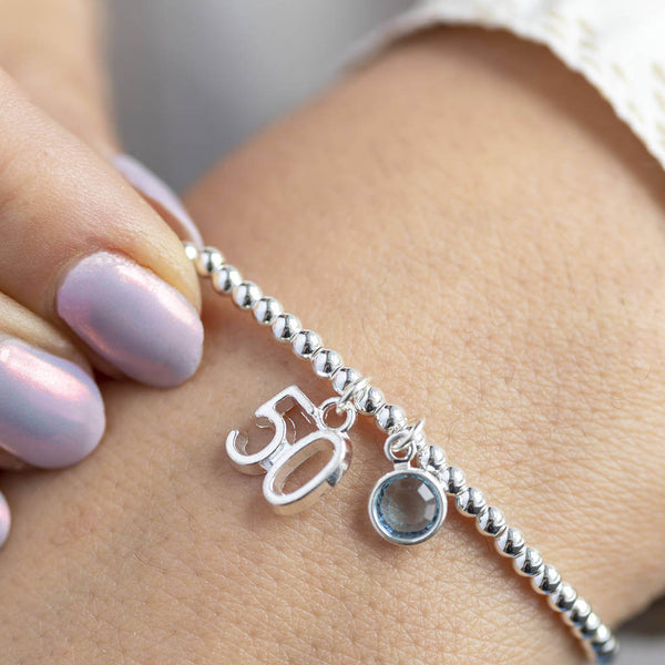 model wears silver plated 50th birthday birthstone charm bracelet with '50' charm and Swarovski birthstone crystal