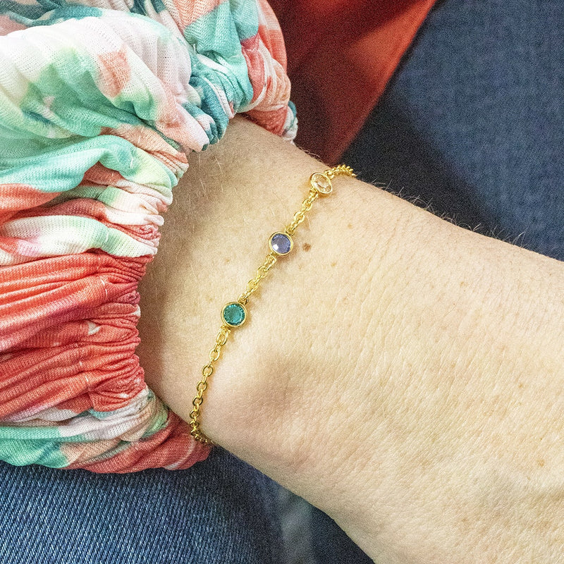 Image show mini gold family birthstone bracelet with three swarovski birthstones in December blue zircon, September sapphire and April crystal.