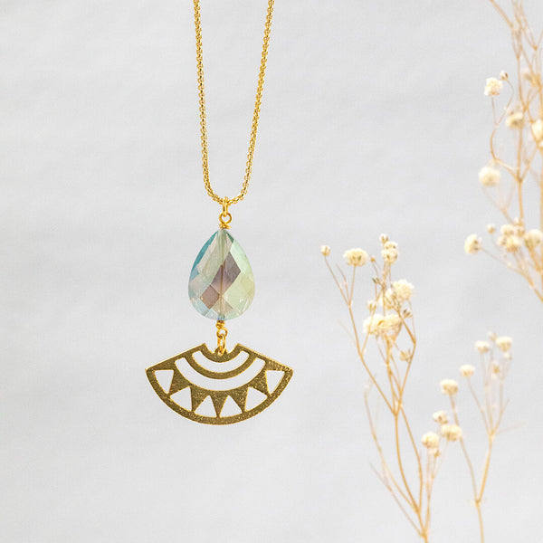 Image shows gold plated long length Andromeda necklace with a blue/green teardrop shaped crystal with a sun ray aztec charm.