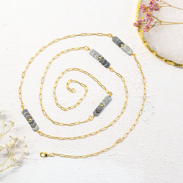 Image shows long length gold plated asteria necklace with four hematite chevron charms throughout. Necklace is spiralled on a white background to show the length and amount of charms. Matching Limited Edition bracelet and earrings available. 