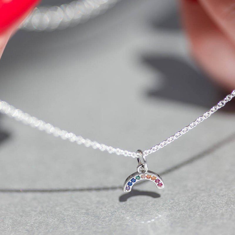 Model holds Silver plated dainty rainbow encrusted necklace. Silver plated necklace has nine tiny crystals in different colours to make the rainbow.