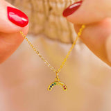 Model holds gold plated dainty rainbow encrusted necklace. Gold plated necklace has nine tiny crystals in different colours to make the rainbow.