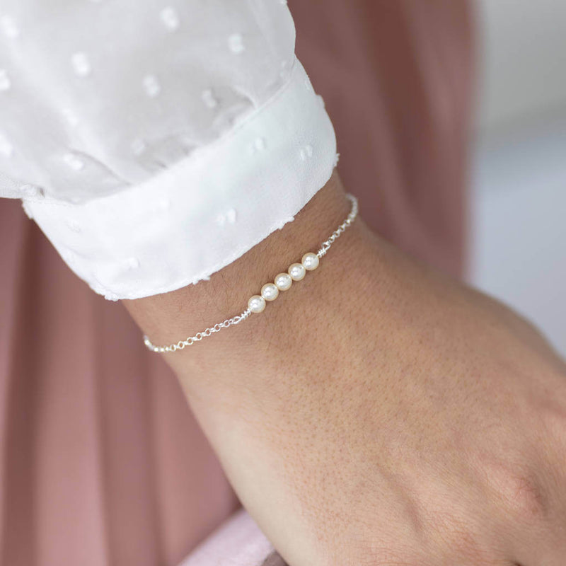 Model wears delicate swarovski pearl bracelet in sterling silver, with five dainty white pearls.