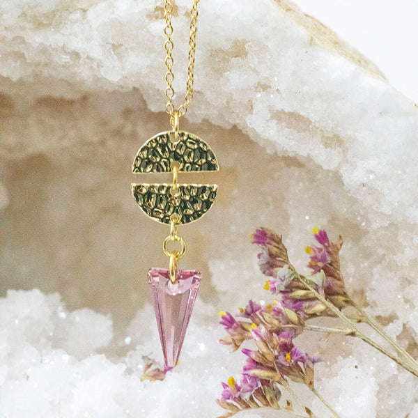 Image shows gold plated ero pink necklace suspended in front of a white crystal