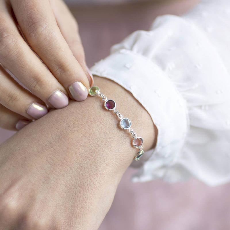 Model wears silver Family Birthstone Link Bracelet with five Swarovski Birthstone Gems (up to 10 can be selected) in Peridot, Amethyst, Aquamarine, Rose and Emerald for August, February, March, October and May.