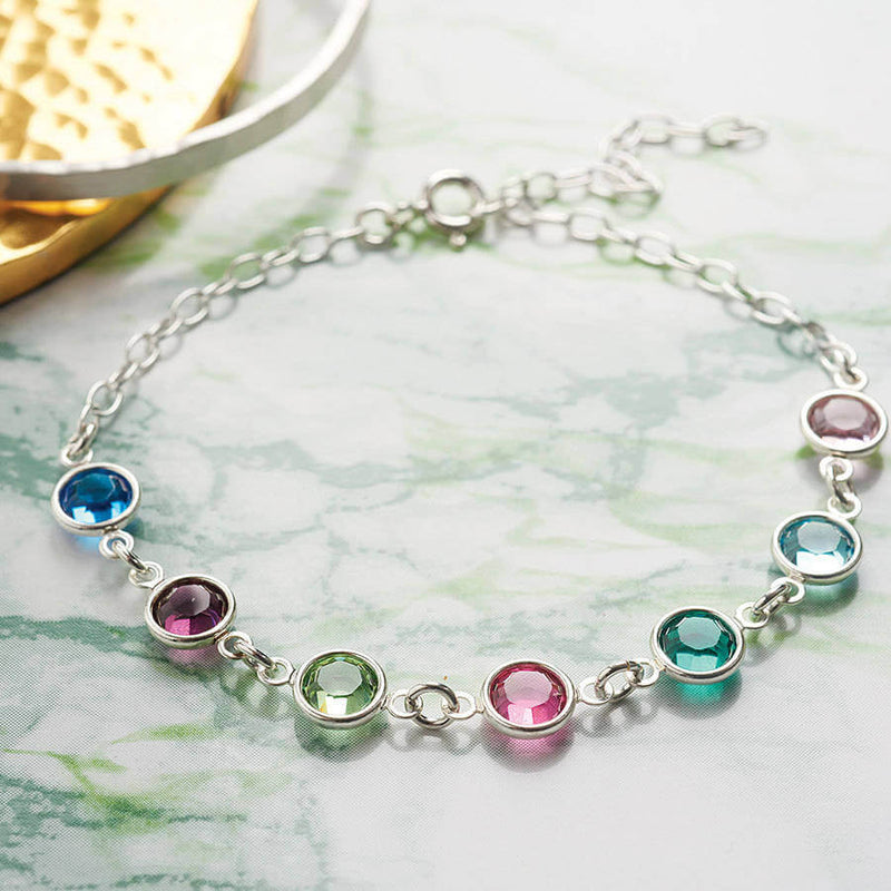Flat lay silver Family Birthstone Link Bracelet with seven Swarovski Birthstone Gems (up to 10 can be selected) in Sapphire, Amethyst, Peridot, Rose, Emerald, Aquamarine, and Light Amethyst for September, February,  August, October, May, March and June.