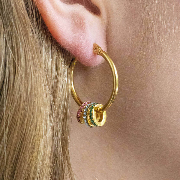 Model wears gold plated birthstone hoop earrings on a white backdrop. Birthstone crystal rings from left to right: October Rose, March Aquamarine, May Emerald.