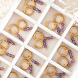 Image shows nine pairs of February amethyst earrings in a jewellery box. Earrings are tiny gold plated huggie hoops with three tiny natural amethyst beads which can be removed.