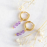 Image shows February amethyst earrings on a white backdrop. Earrings are tiny gold plated huggie hoops with three tiny natural amethyst beads which can be removed.
