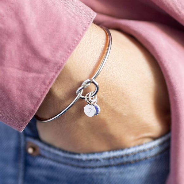 Model wears silver plated Friendship Knot Bangle with a small disc initial charm with the letter 'J' and a small amethyst Swarovski birthstone charm for the month of February.