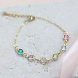 Image shows gold family swarovski birthstone link bracelet. Birthstones from left to right: December blue zircon, June light amethyst, April crystal, August peridot, March aquamarine and october rose. Bracelet is on a pale grey backdrop. 