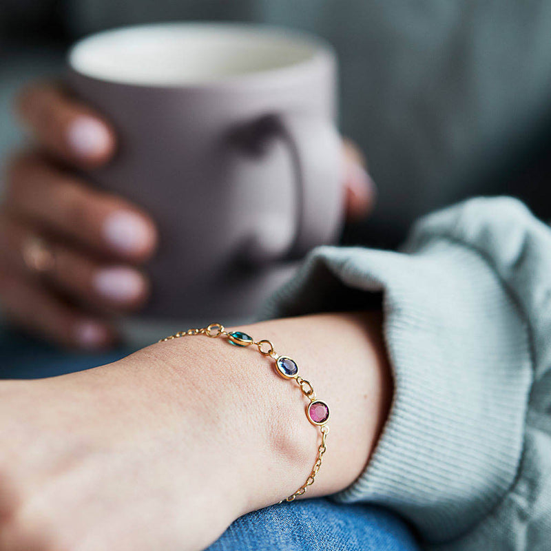 Model wears gold family swarovski birthstone link bracelet.Visible birthstones from left to right: May emerald, September Sapphire and October Rose.