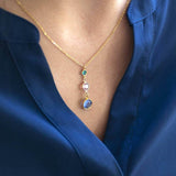 Model wears Gold Three Generations Birthstone Pendant Necklace. Swarovski birthstones arranged from bottom to top in selection order: September Sapphire, April Crystal, December Blue Zircon.