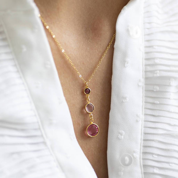 Model wears Gold Three Generations Birthstone Pendant Necklace. Swarovski birthstones arranged from bottom to top in selection order: October Rose, June Light amethyst  and February Amethyst.