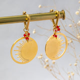 Image shows gold plated Hinia triangle huggies with red swarovski crystal clusters hanging from a golden display.