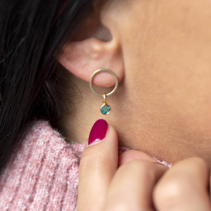 Model wears minimalist gold circle birthstone earrings with a December Blue Zircon Birthstone.