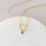 Image shows minimalist gold circle birthstone necklace with September Sapphire Swarovski birthstone charm on a white backdrop.