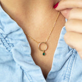Model wears minimalist gold circle birthstone necklace with May Emerald Swarovski birthstone charm.