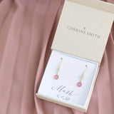 Image shows gold plated mother and child birthstone earrings displayed in a JOY gift box on a pink backdrop. Earrings show March aquamaring birthstone for child and October Rose pink to represent mother.