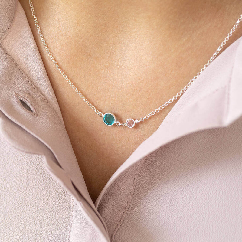 Image shows model wearing Mother and Child Birthstone Link Necklace in sterling silver. Birthstones from left to right for mother and child - May green emerald and April clear crystal.